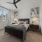 A bedroom with a bed and wall decor, large window, ceiling fan, carpet flooring