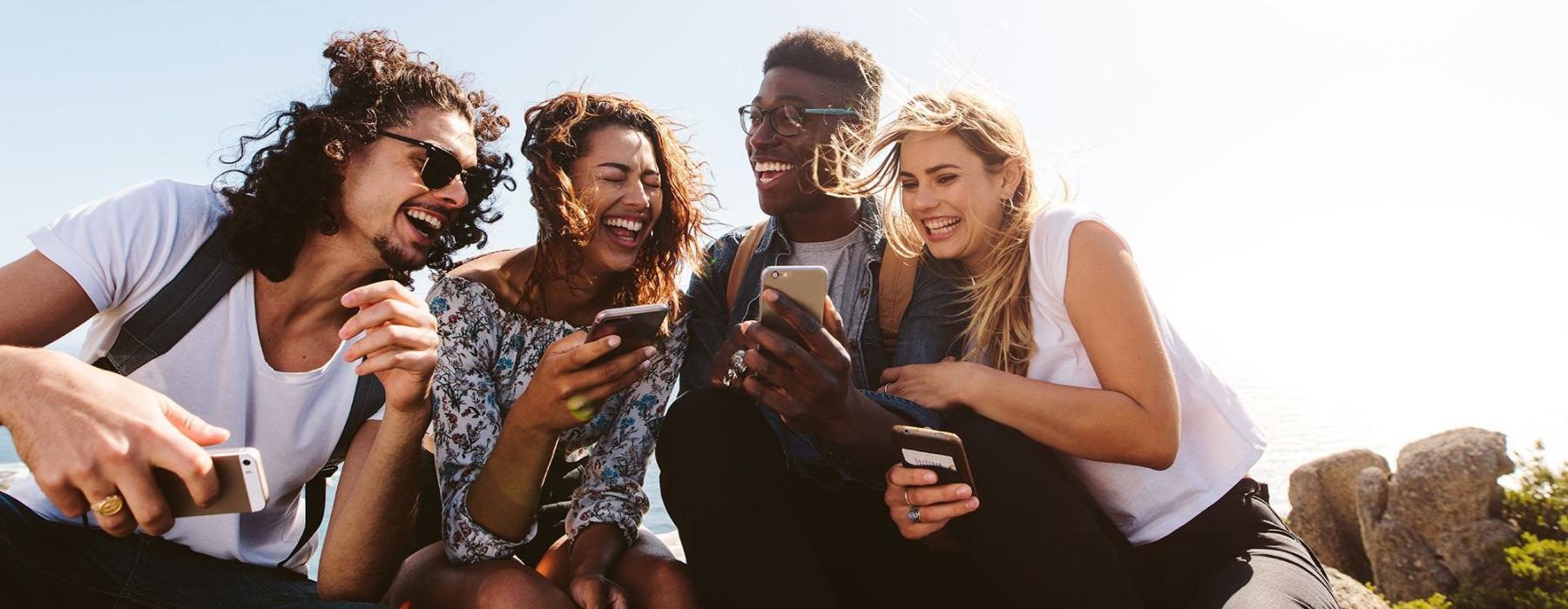 a group of friends sit outside laughing over their cell phones